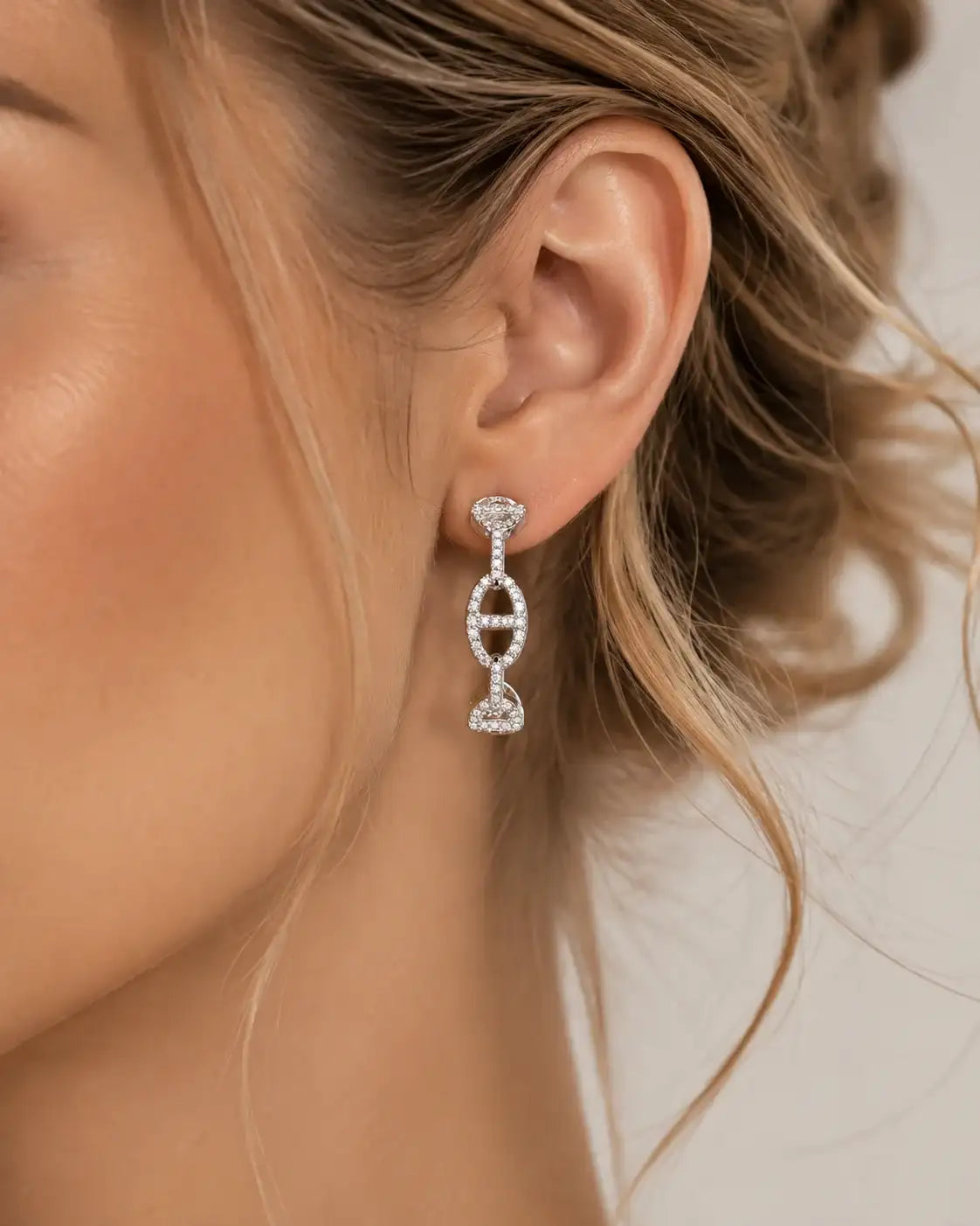 Boucle d'oreille pendante en argent pavée de zircons portée par une femme aux cheveux blonds